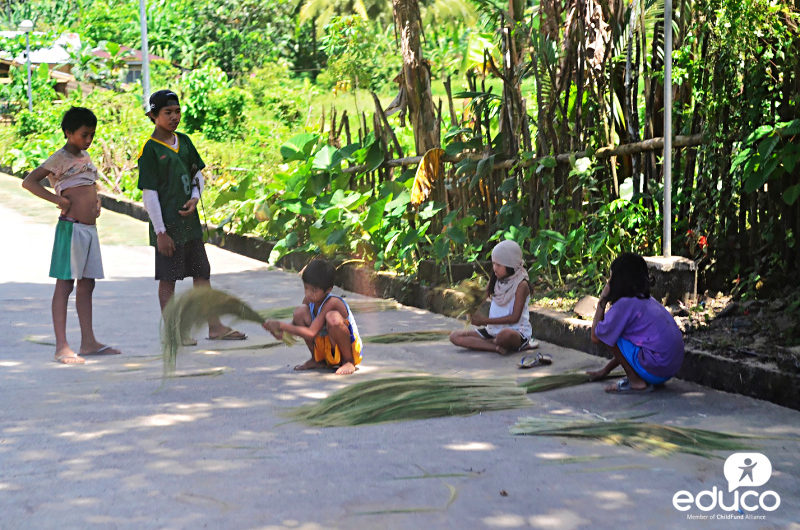 Children making Filipino brooms (walis ting-ting) made out of grass in Catanduanes.