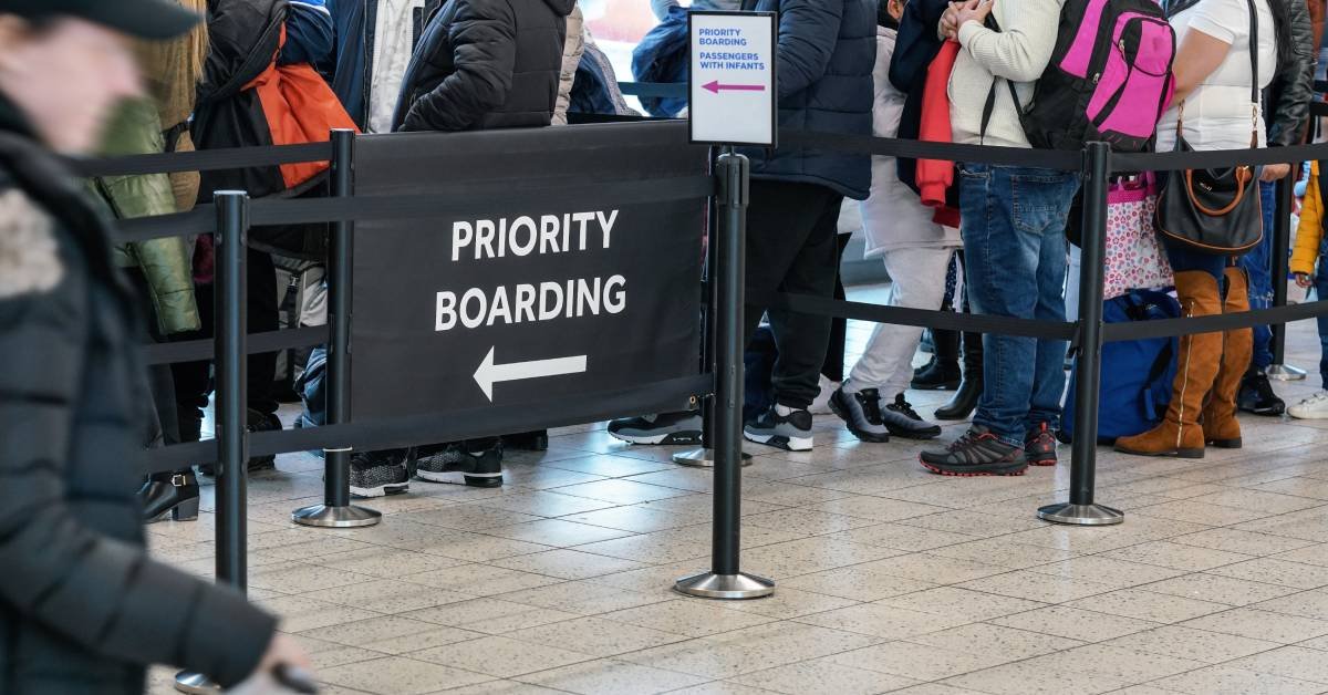 An airport gate with people standing in line and a priority boarding sign with an arrow placed at the entrance.