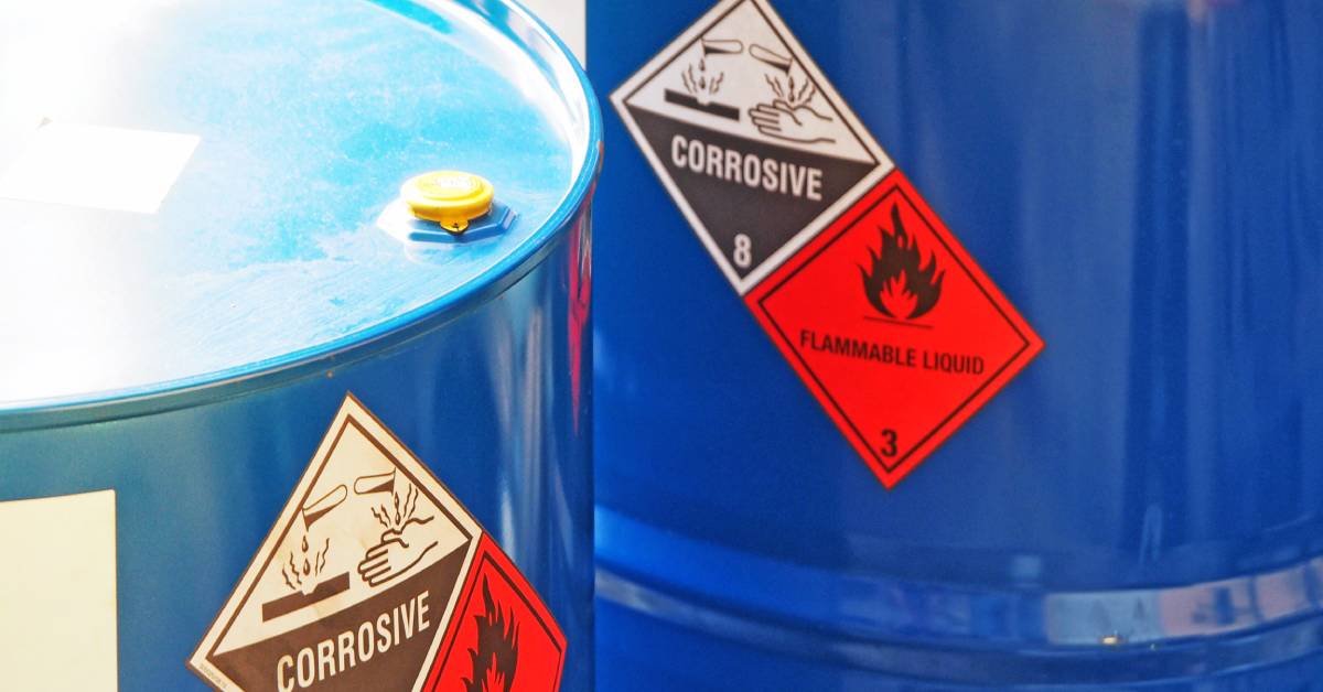 Two bright blue hazardous waste barrels with yellow caps display stickers that say "corrosive" and "flammable liquid."