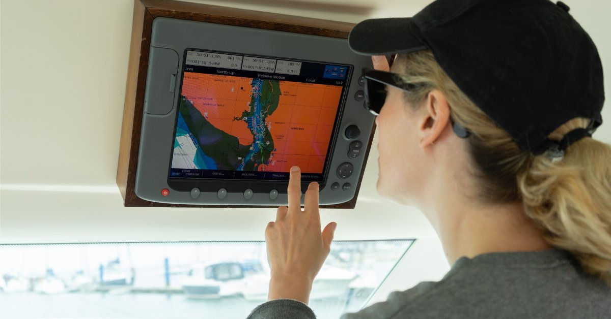 A blonde-haired woman wearing black sunglasses and a black hat touches a navigational system’s screen.