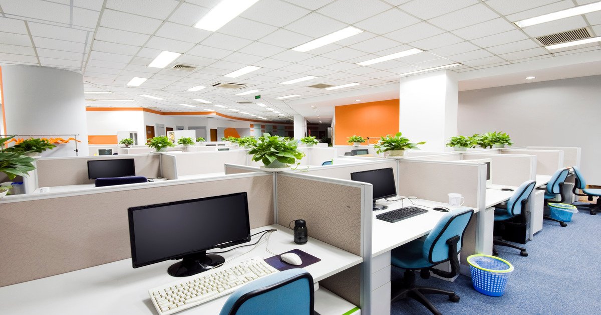 A large office is filled with workstations. Each desk has a grommet for cables from computer mice, monitors, and keyboards.