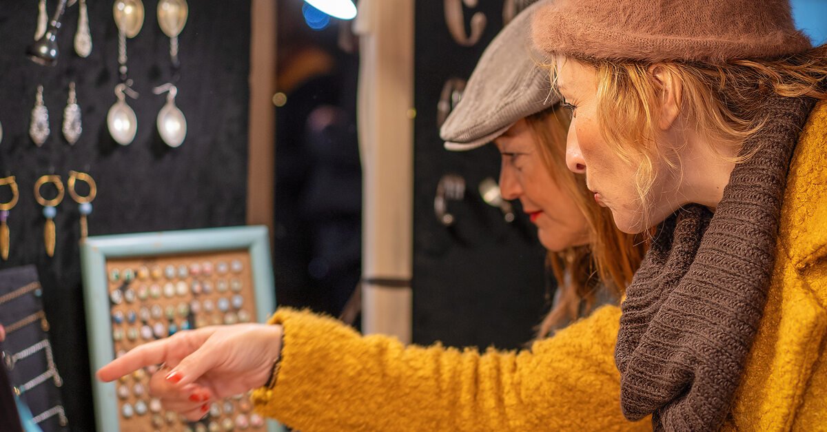 Two women browsing jewelry and accessories together at a booth. One woman points to products, while the other observes.