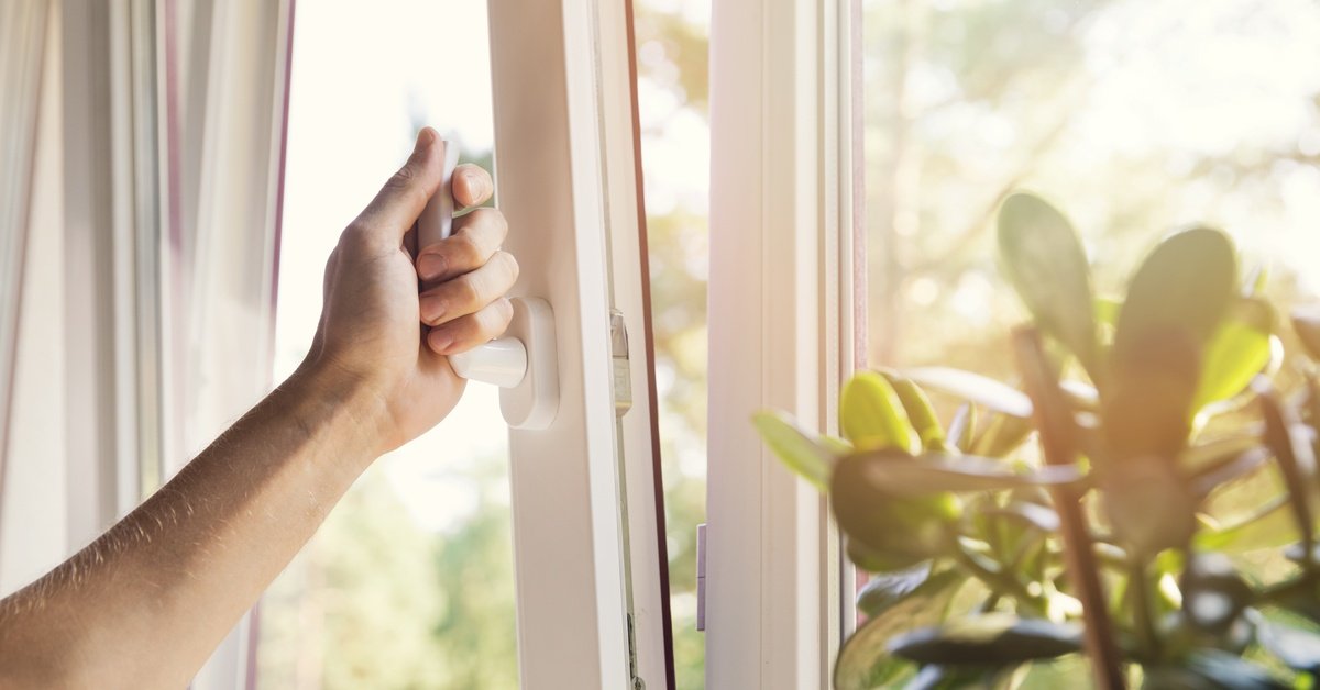A person grabbing the handle of a top-opening window and pulling the window open on a nice day.