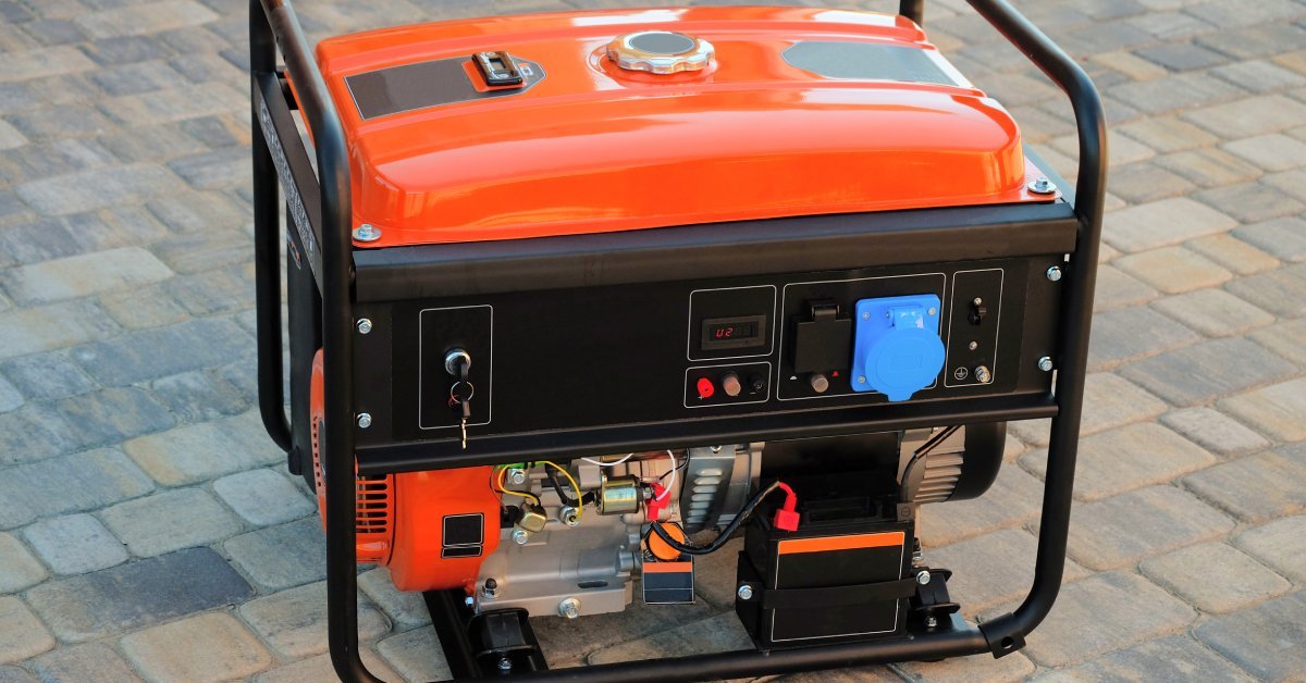 An orange-and-black portable generator sitting on a brick walkway. It has a key in the starter and a blue fuel cap.