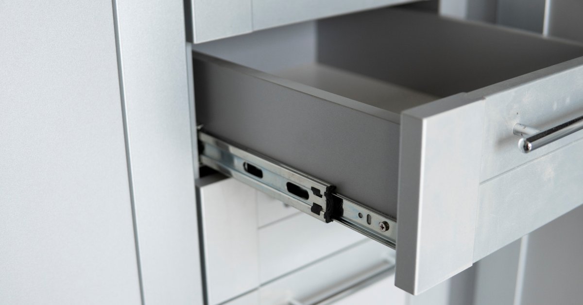 A close-up of an extended drawer in gray cabinetry. A stainless steel side-mounted drawer slide is visible.