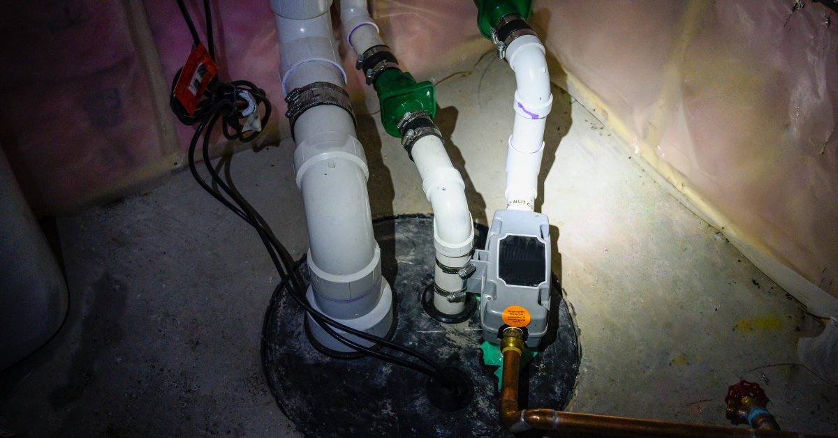 A flashlight is shined into a manhole, leading to a sump pump backed up with water in the basement of a house.