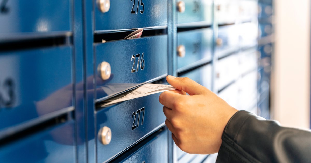 A close-up of someone's hand putting paper in a dark blue mailbox with the number 277 on it in a condominium house.