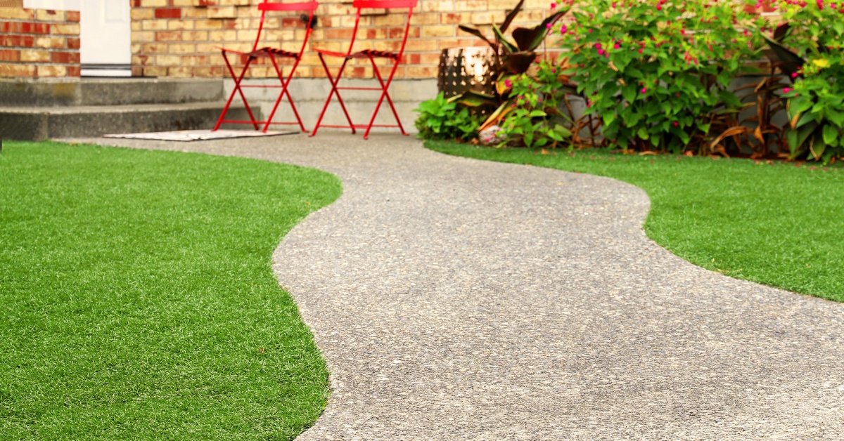 A home features landscaping with artificial grass and a path. Two red lawn chairs sit outside the house.