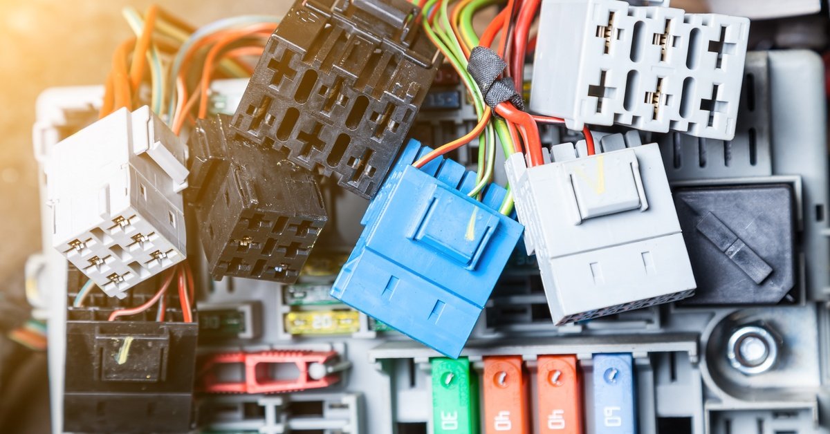 A small white car driving down the road at nighttime. The car’s headlights are illuminated with a bright white light.