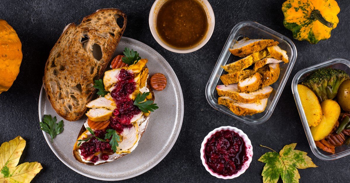 A close-up of a turkey sandwich made with leftovers from a Thanksgiving meal or a large dinner with pumpkins on the table.