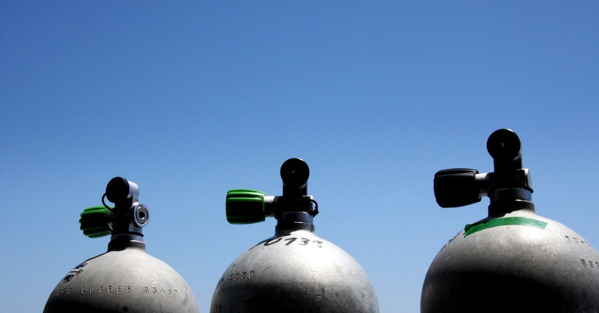 Three cylindrical gas canisters are lined up in a row. The bright, blue sky appears behind the containers.