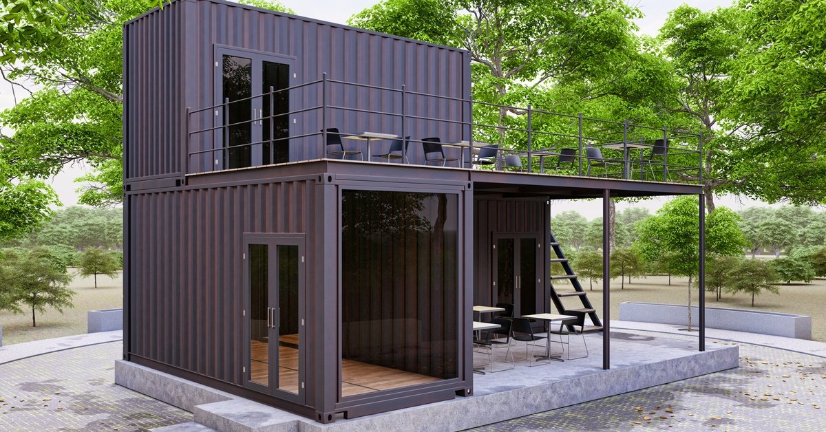 A two-story container office with glass walls, rooftop deck, outdoor seating, and stairs surrounded by green trees.