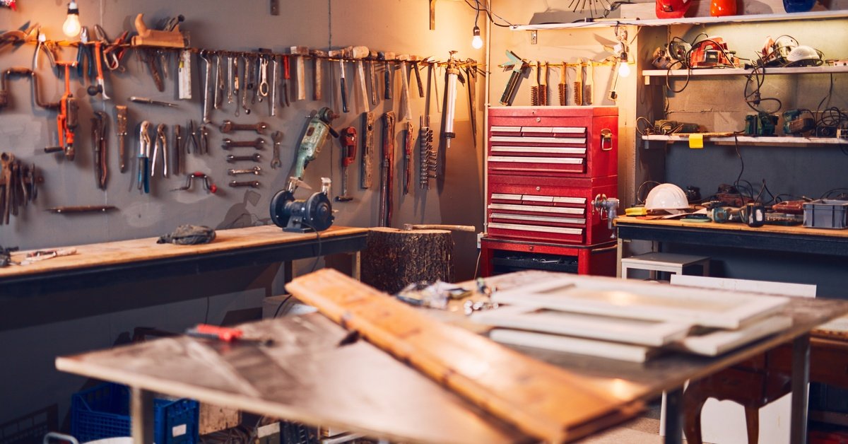 A workshop with many tools attached to the walls as well as lying on tables. There is a red tool box in the back.