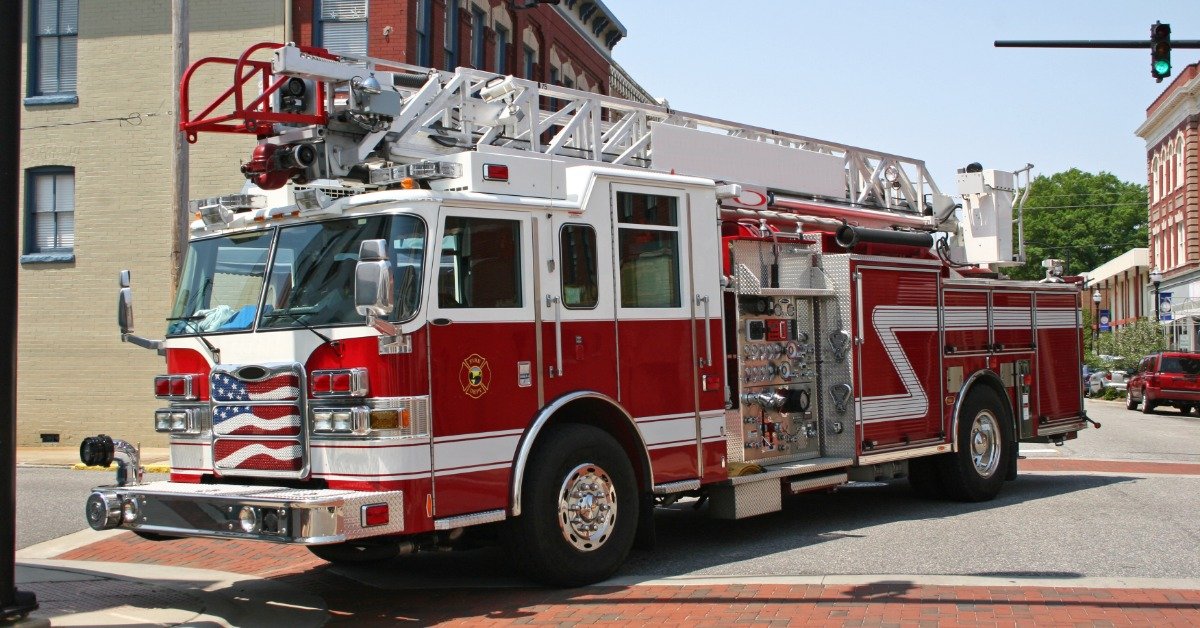Red and white fire truck stopped at a downtown intersection with an extended aerial ladder mounted on top.
