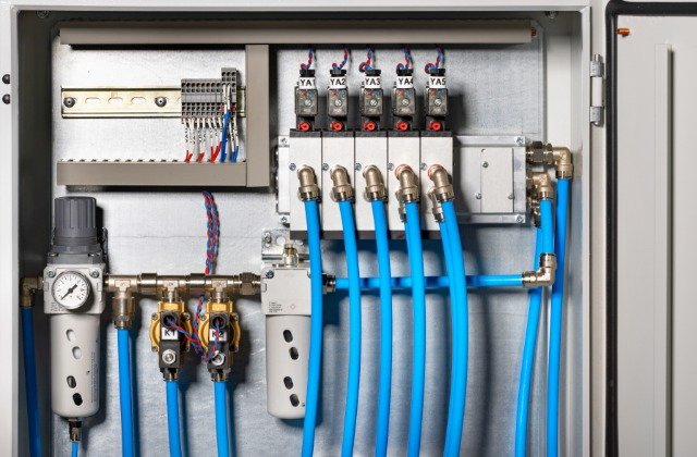 Open pneumatic control cabinet with five labeled valves, blue air hoses, electrical wiring, gauges, and regulators.