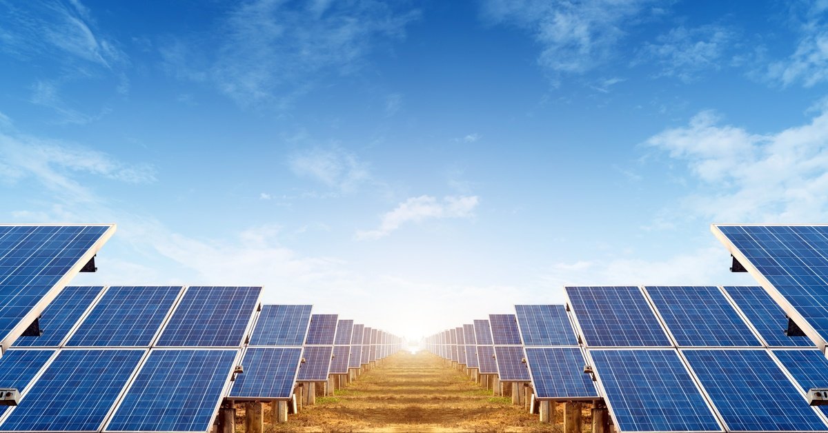 Ground-mounted solar panels form parallel rows under a clear blue sky with the sun shining at the horizon.