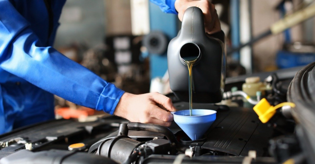 Mechanic pours fresh motor oil through a blue funnel into a car engine during routine maintenance in a repair shop.