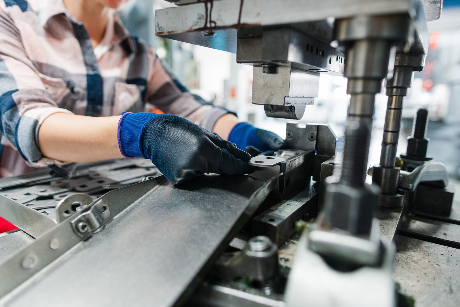 A person wearing gloves placing a small metal part on a punching machine inside a bright factory workspace.