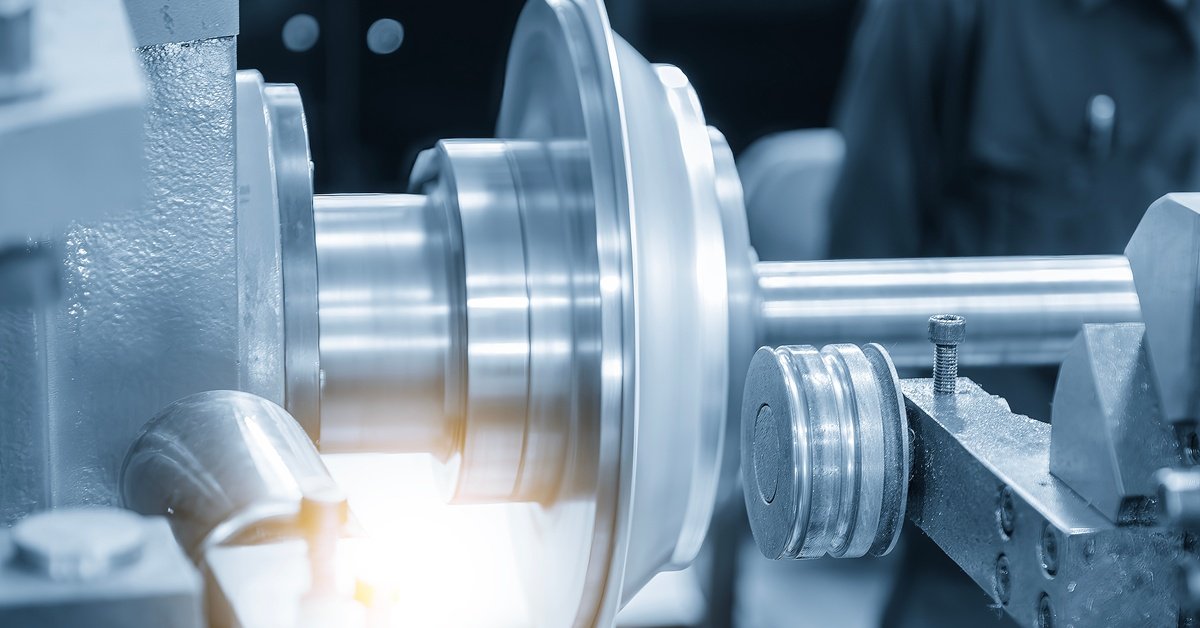 Close-up of a shiny metal shaft and rotating disc on an industrial machine, with a grooved roller positioned beside it.