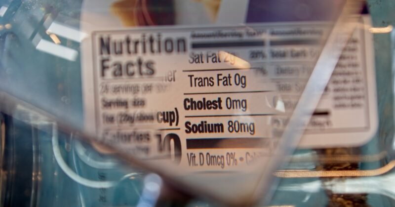 The nutrition facts label of a box, focusing on cholesterol and sodium, partially expanded by a magnifying glass.
