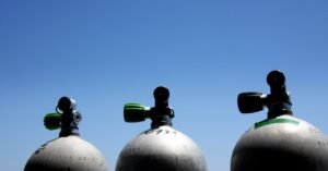 Three cylindrical gas canisters are lined up in a row. The bright, blue sky appears behind the containers.