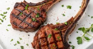 Two perfectly grilled Bone-In Ribeyes with crosshatch marks, garnished with fresh herbs on a white plate for date night dinner.