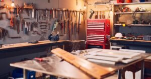 A workshop with many tools attached to the walls as well as lying on tables. There is a red tool box in the back.