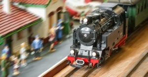 A model of a steam train driving into a model train station. There are tiny model people waiting for the train.