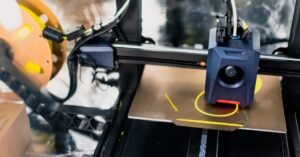 3D printer extrudes bright yellow filament onto a metal print bed as the print head builds a prototype layer by layer.